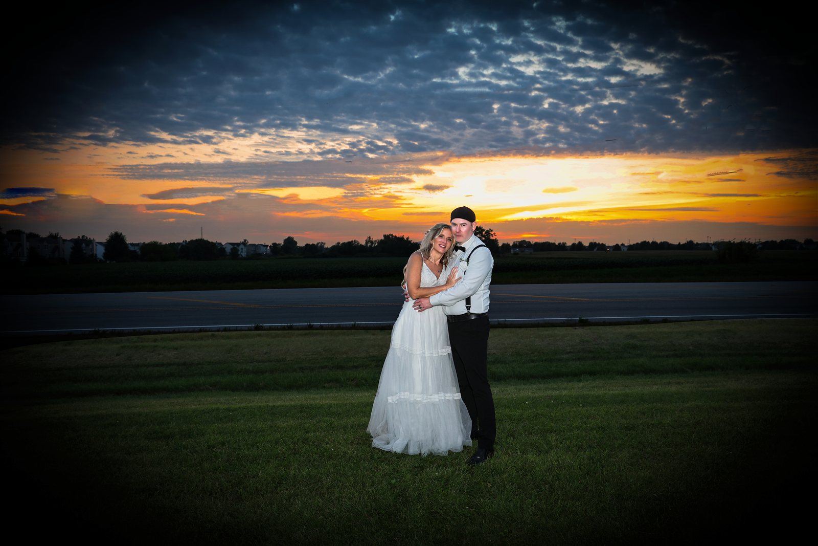 Newlyweds embracing outdoors beneath an orange sunset and dramatic clouds