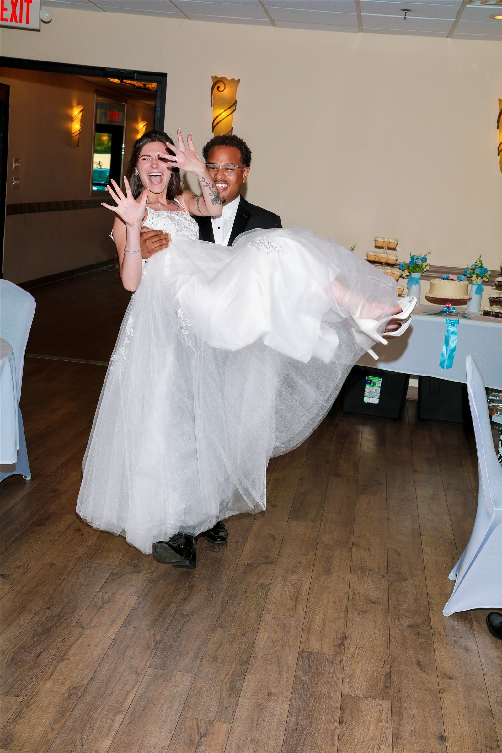 Groom carrying a laughing bride beside the wedding reception dessert table
